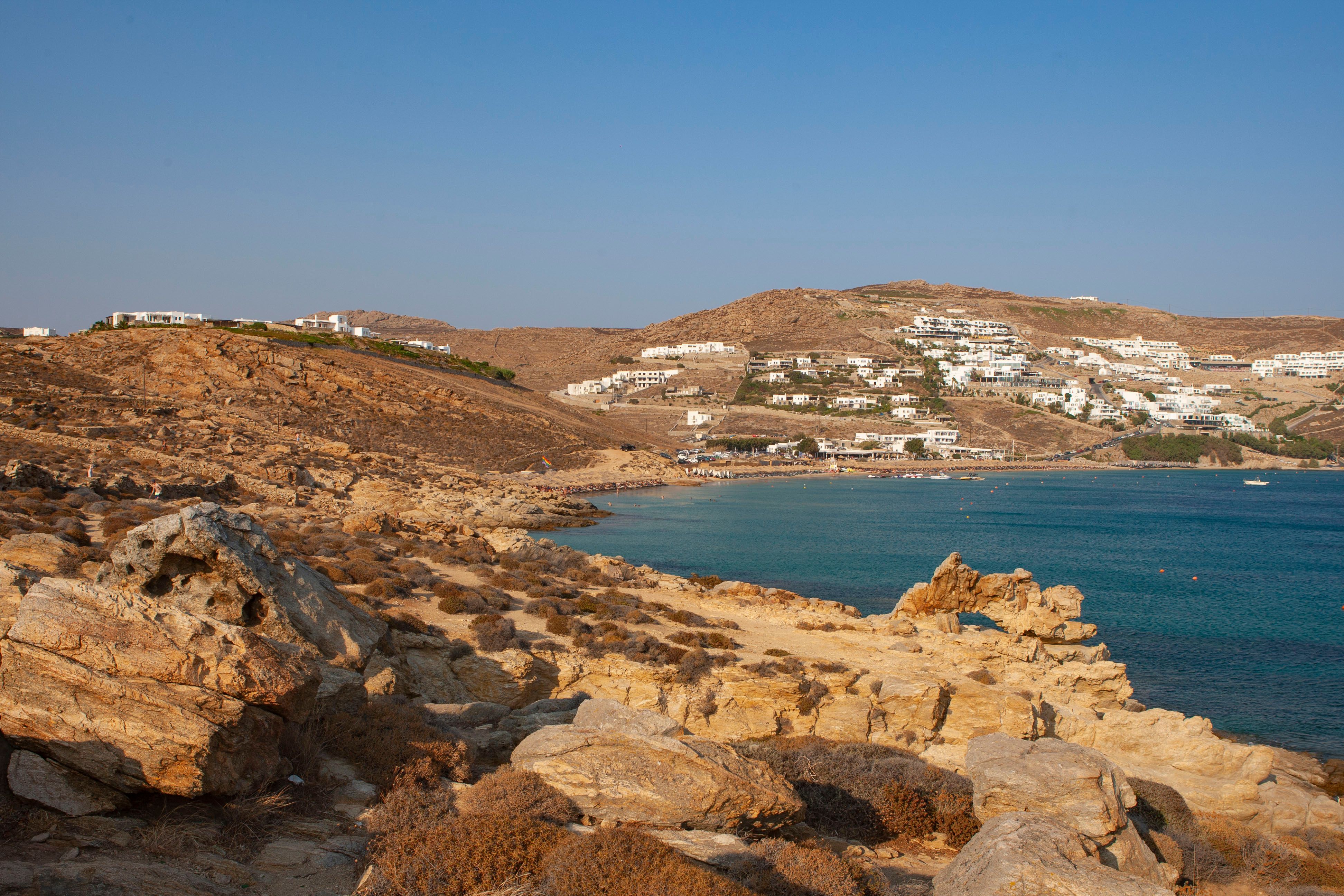 Sunny beach scene in Mykonos, Greece, with clear blue water and sunbathers