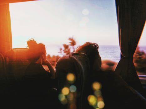 Two people enjoying a scenic bus ride during sunset, capturing a serene ocean view.