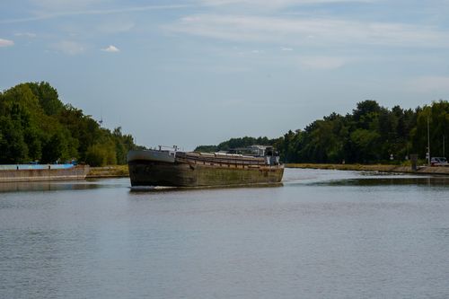 Free Cargo barge navigating through a peaceful waterway in Dessel, Belgium surrounded by lush greenery. Stock Photo