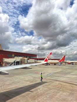 Airplanes parked at the terminal with a worker directing on a sunny day with clouds.