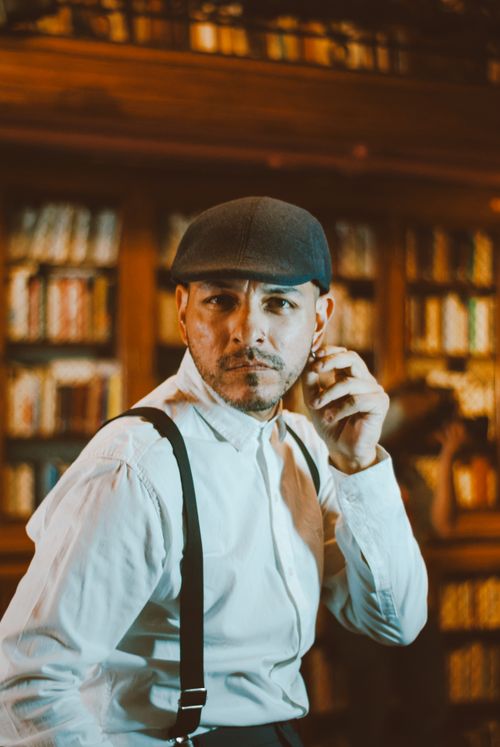 Free Portrait of a vintage styled man wearing a cap and suspenders in a classic library. Stock Photo