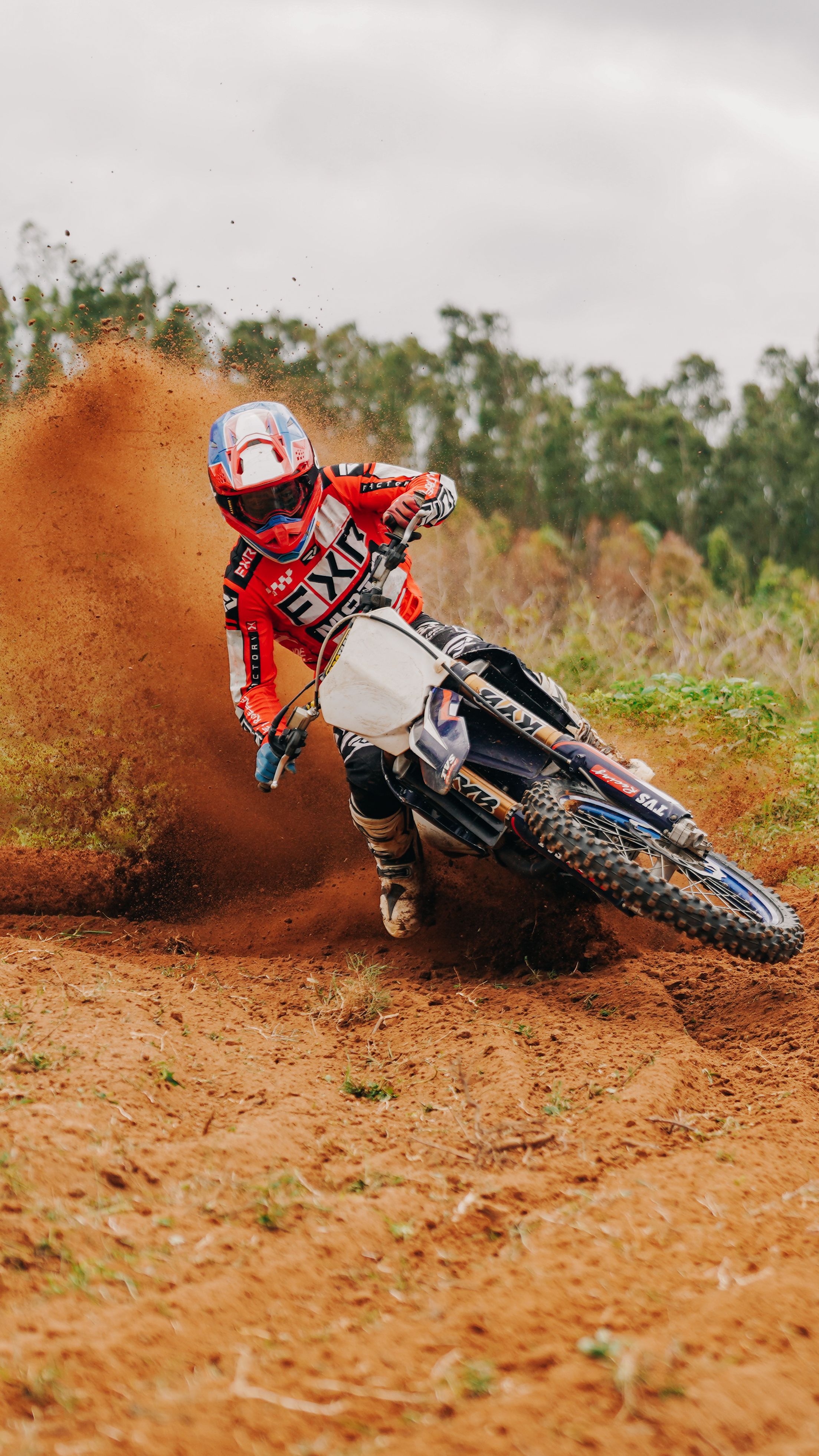 Rider on motocross bike making sharp turn on dirt track, creating dynamic dust cloud.