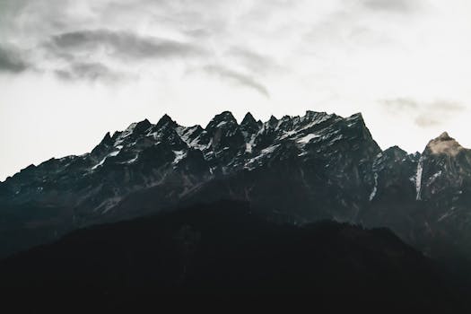 A breathtaking landscape of rugged, snow-capped mountains under a moody, overcast sky.