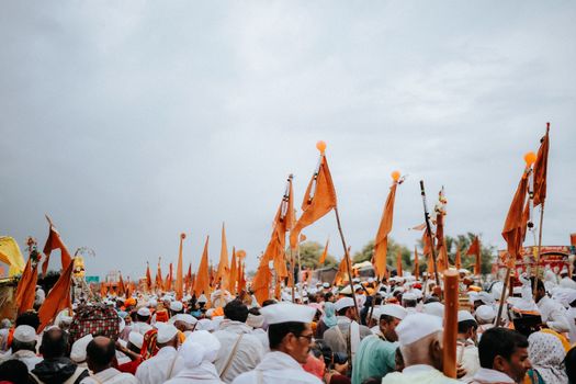 Colorful outdoor procession with a crowd holding orange flags, creating a festive atmosphere.
