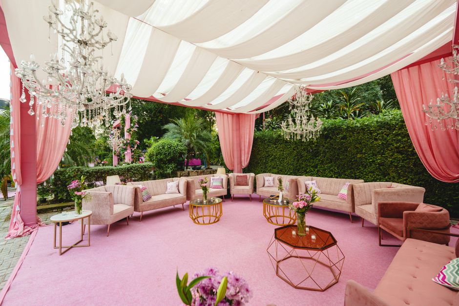 Luxurious outdoor lounge setup with pink drapery and chandeliers, perfect for weddings or events.