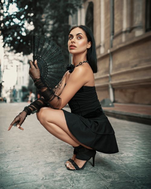 Free Sophisticated woman squatting on cobblestone street in stylish black outfit. Stock Photo