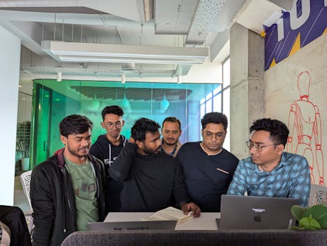 A group of coworkers collaborating with laptops and notebooks in a modern office space.