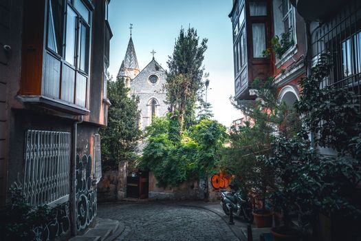 A picturesque view of a narrow Istanbul alley leading to a historic stone church framed by greenery.