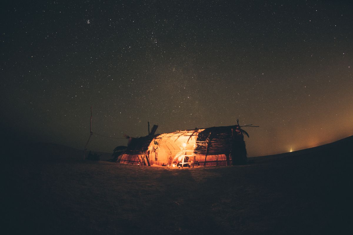 A desert camp glowing under the Wadi Rum night sky — the Milky Way visible here as a textured band, not a photographic effect.