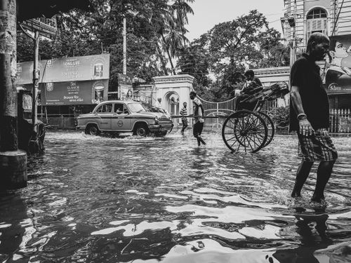 Free A bustling street in Kolkata, India, during monsoon floods with rickshaws and pedestrians. Stock Photo