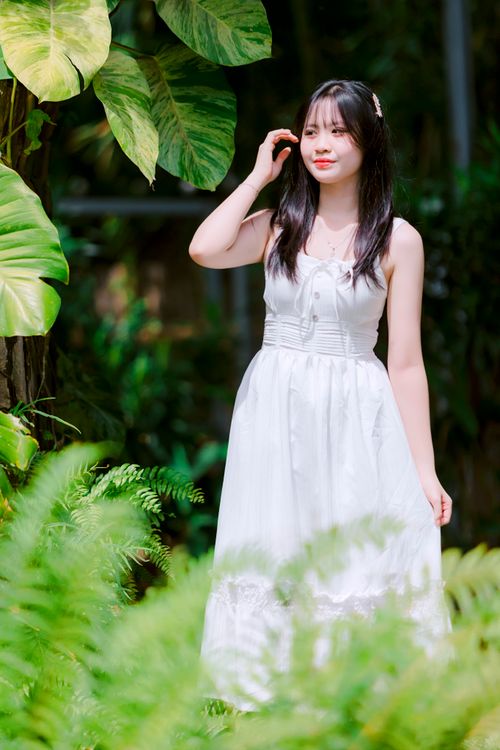 Free Elegant woman in a white dress surrounded by vibrant green foliage, enjoying a sunny day outdoors. Stock Photo