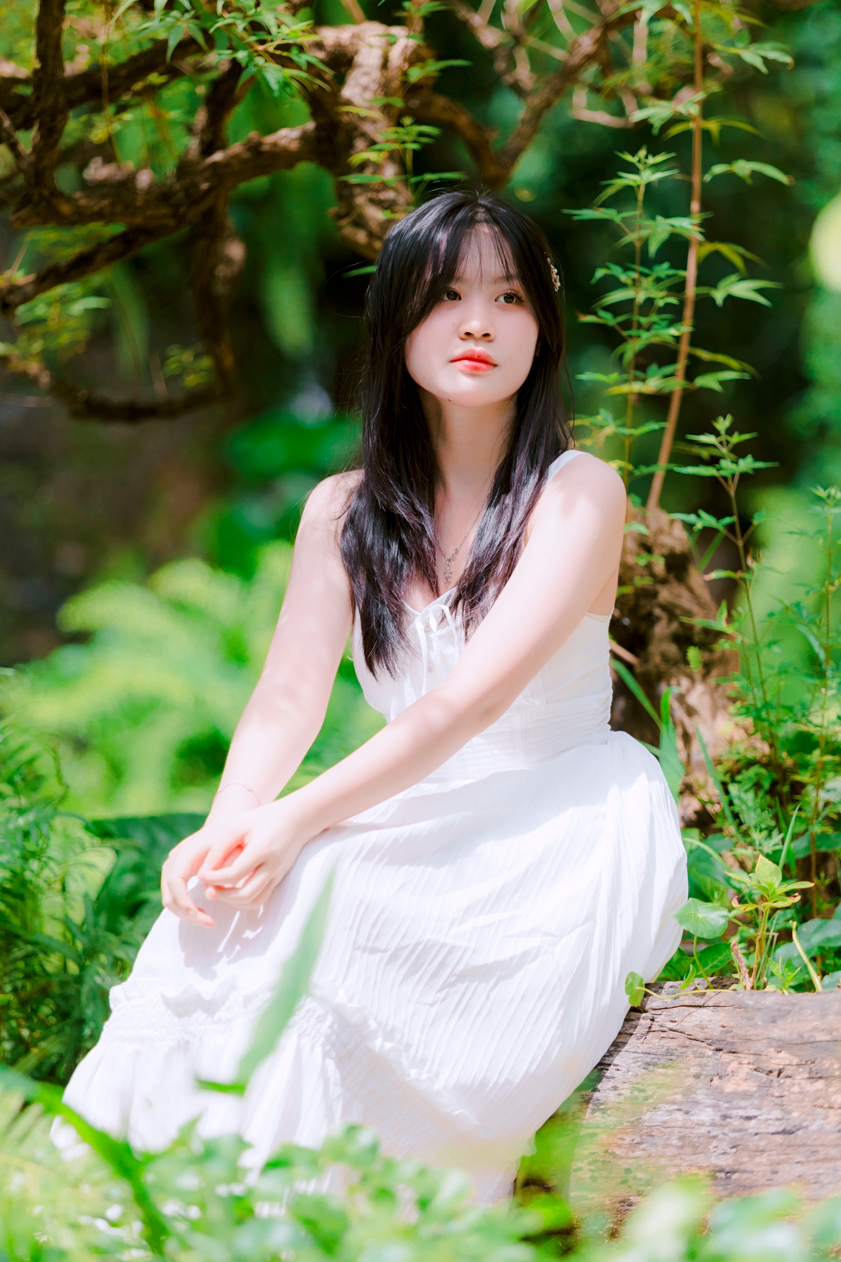 A serene portrait of a young woman in a white dress sitting in a vibrant green forest.