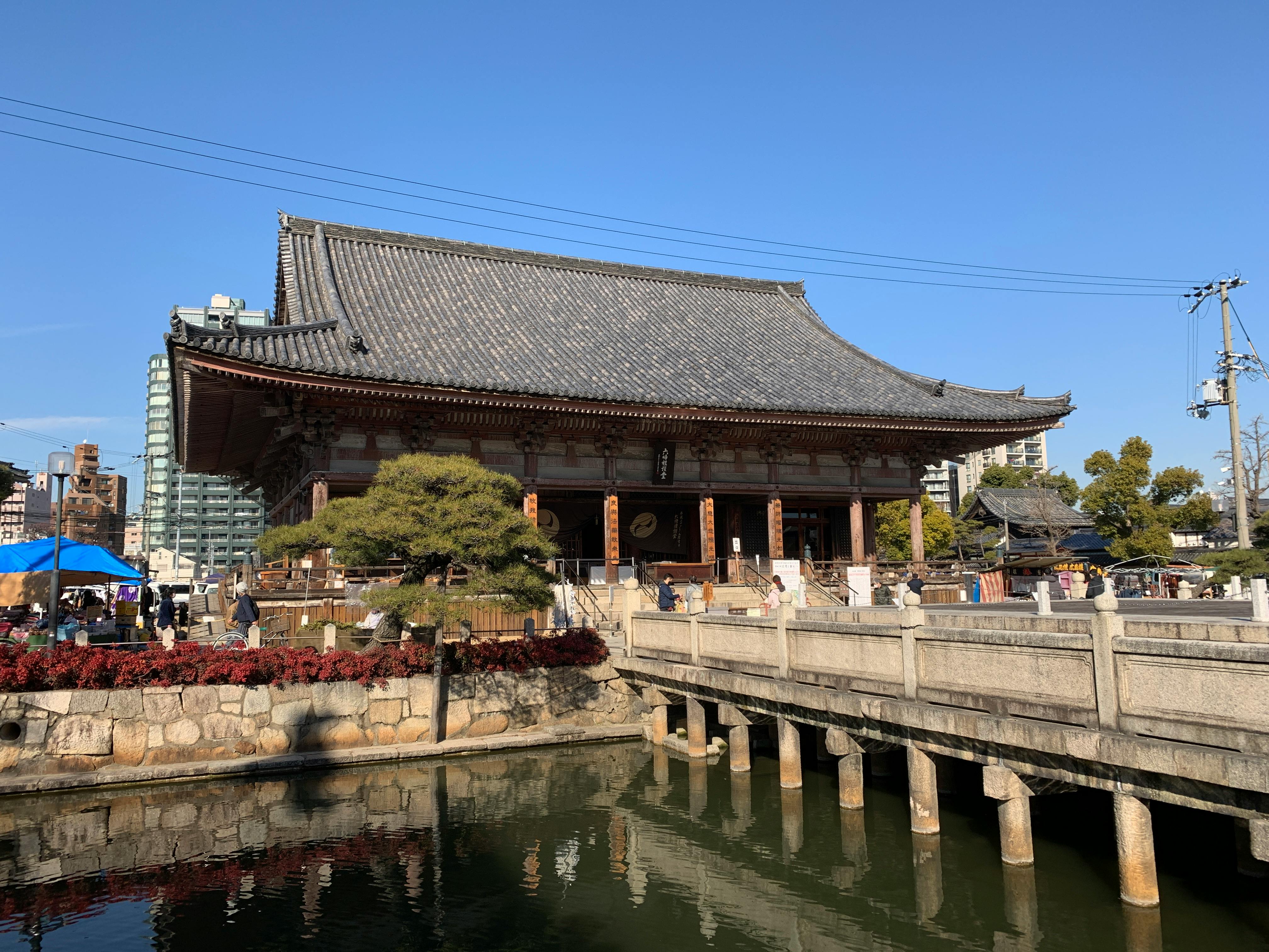 Explore the historic Shitennoji Temple in Osaka, Japan, with its traditional architecture and serene reflection on a sunny day.