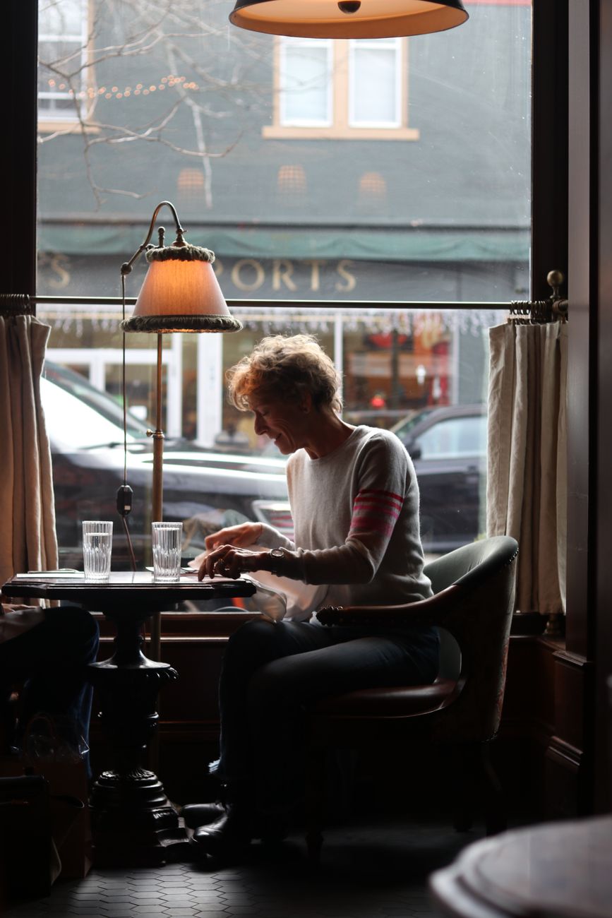 Woman enjoying a quiet moment in a New York City cafe, captured through a window.
