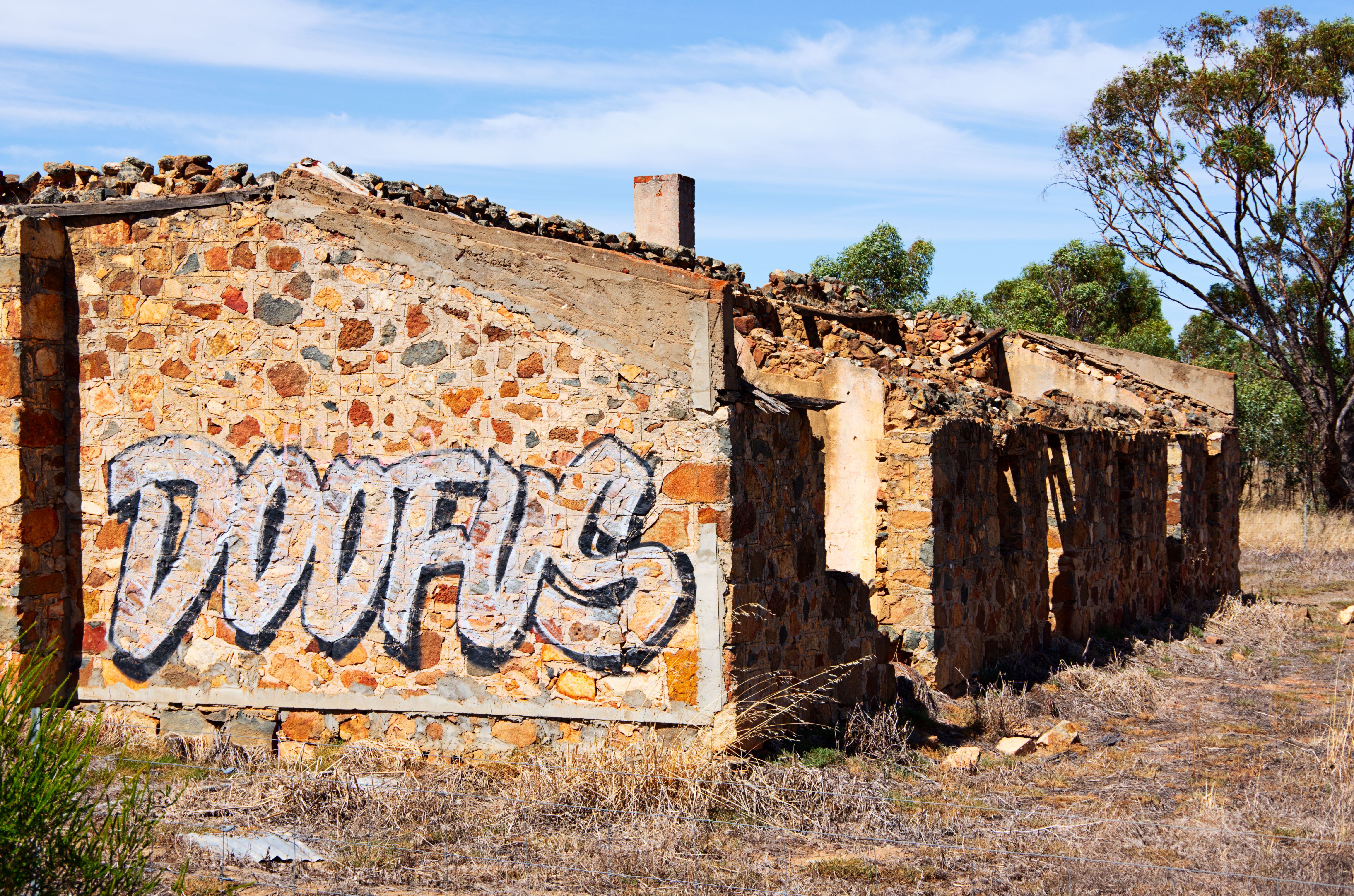 Stone ruin with graffiti in rural Australia under a clear blue sky.