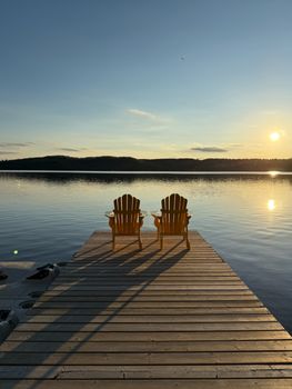 Peaceful sunrise view over lake with empty wooden chairs on a dock at Dwight, Ontario.