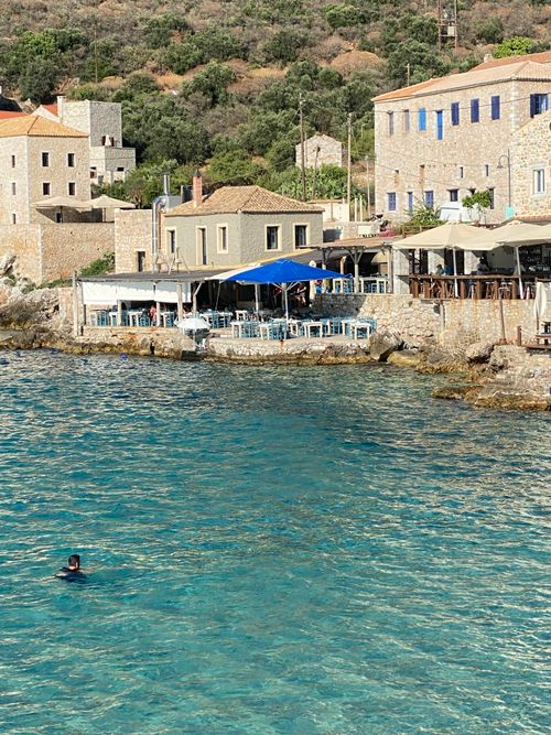 Free Serene coastal view of a Greek village with waterfront dining and clear blue waters. Stock Photo