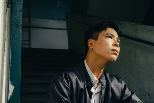 Free A young man looks thoughtfully toward natural light in a dim stairwell. Stock Photo
