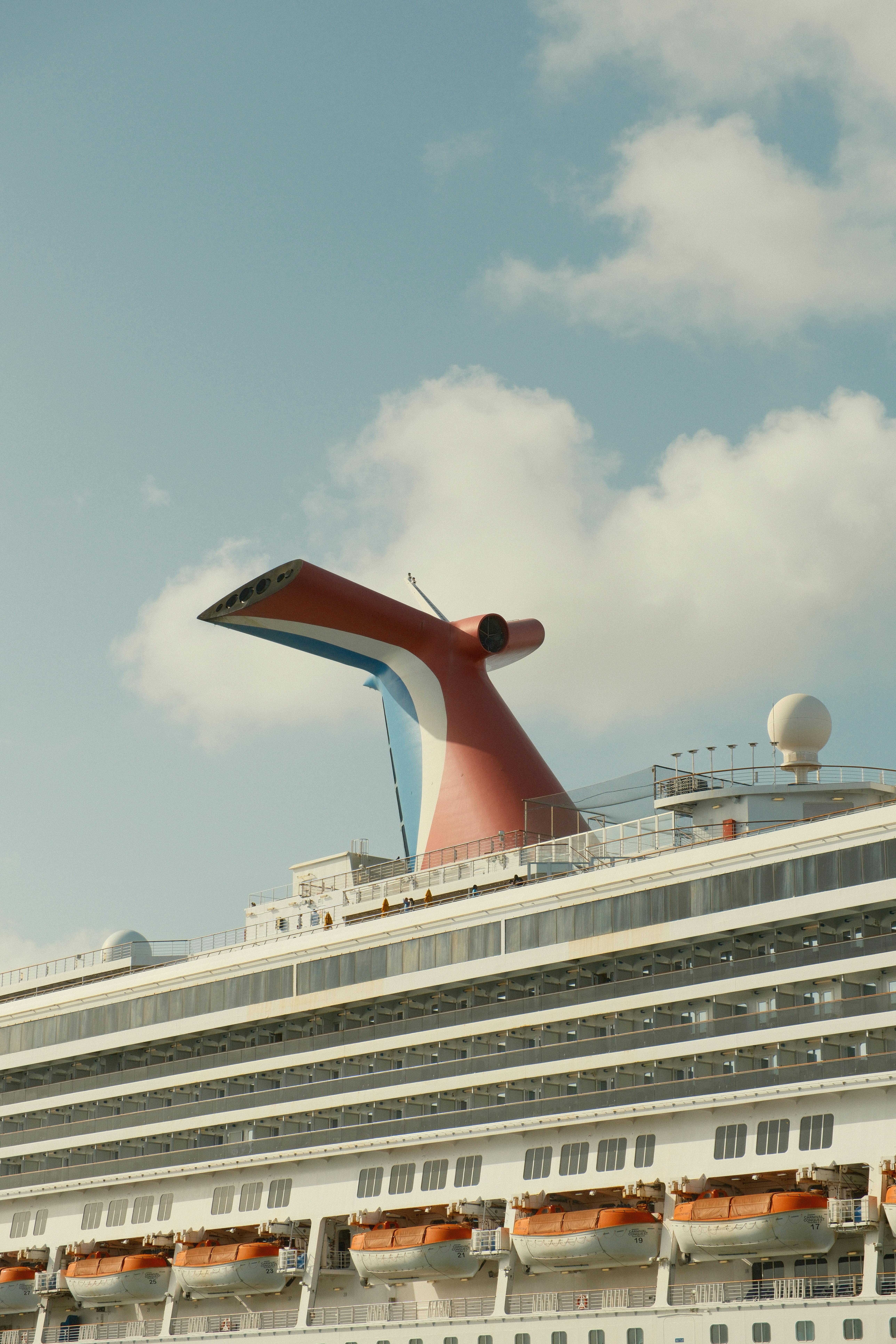 Elegant cruise ship with distinctive red funnel under a clear blue sky.