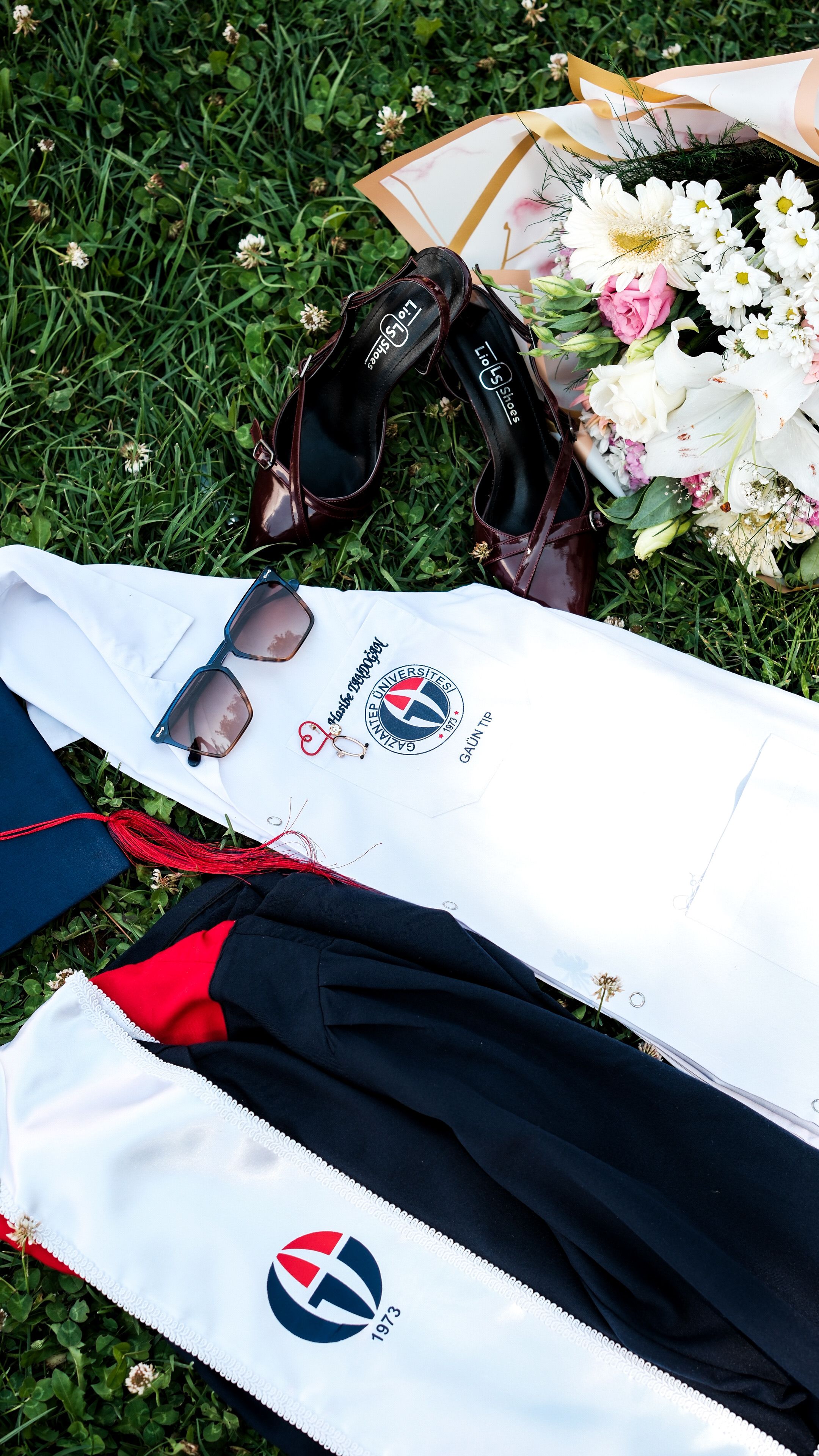 Top view of graduation attire and flowers on grass in Gaziantep, Türkiye.