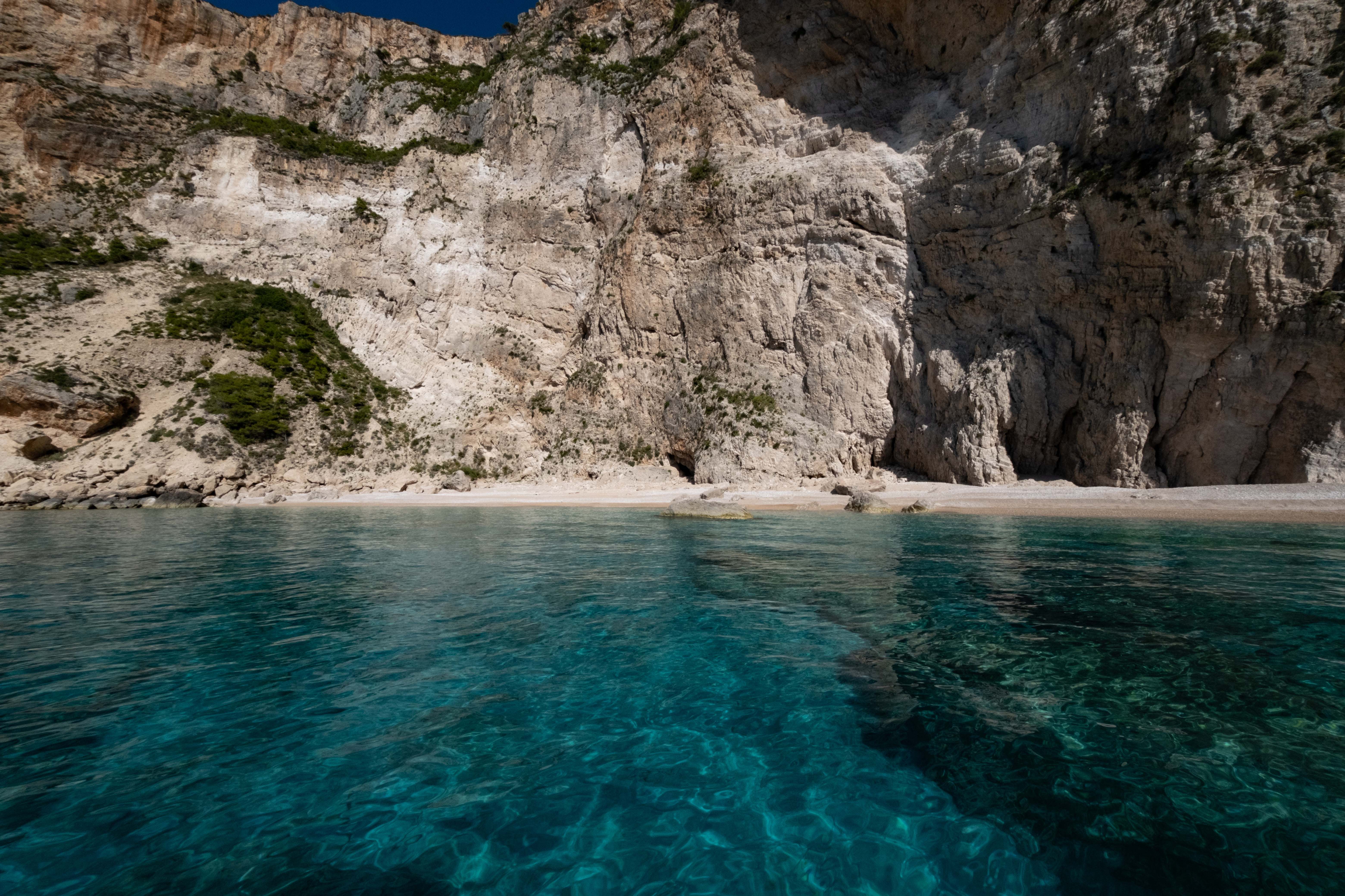 Crystal Clear Coastal Beach and Rocky Cliff · Free Stock Photo