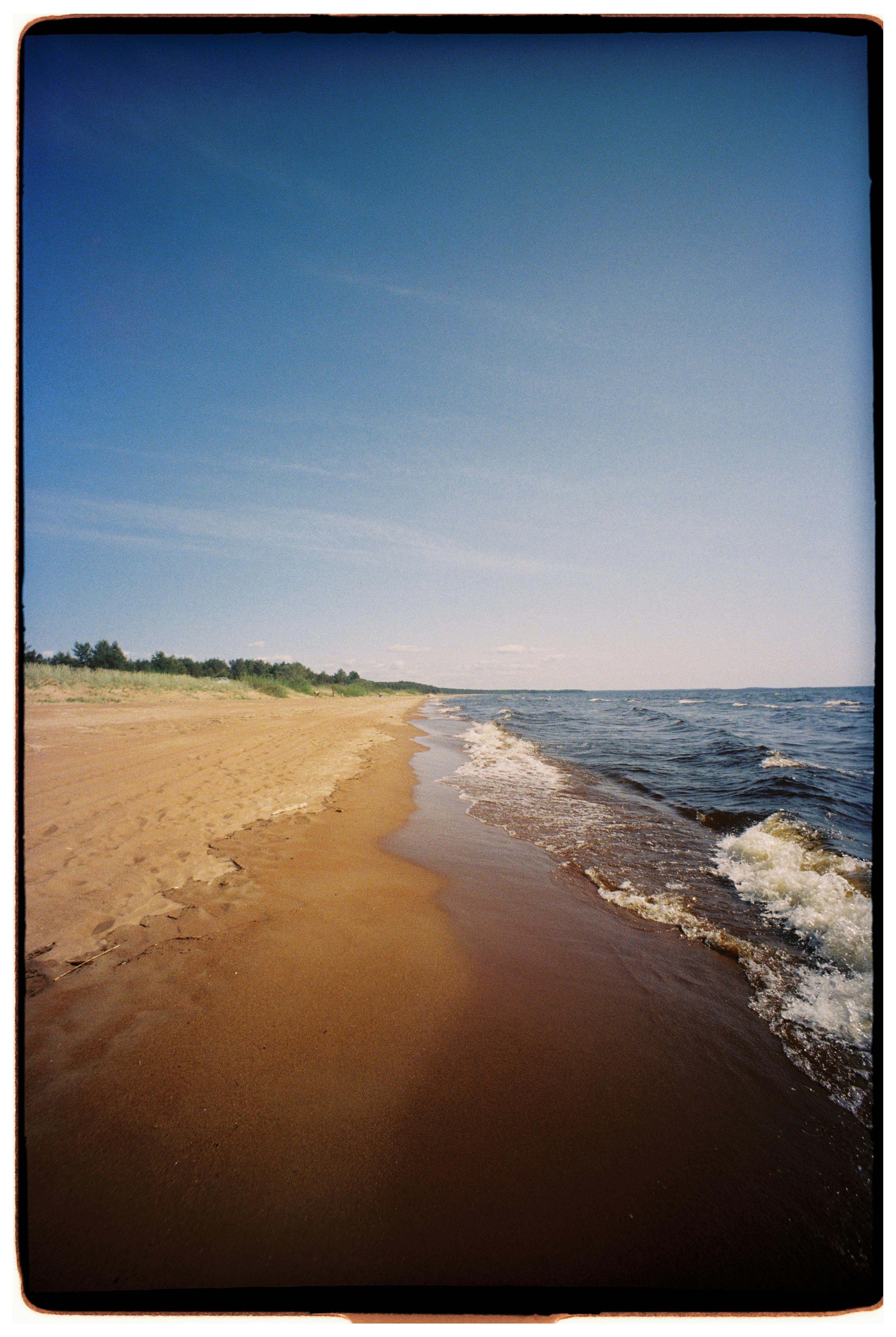 Peaceful sandy beach with gentle waves and clear blue sky, perfect for a summer escape.