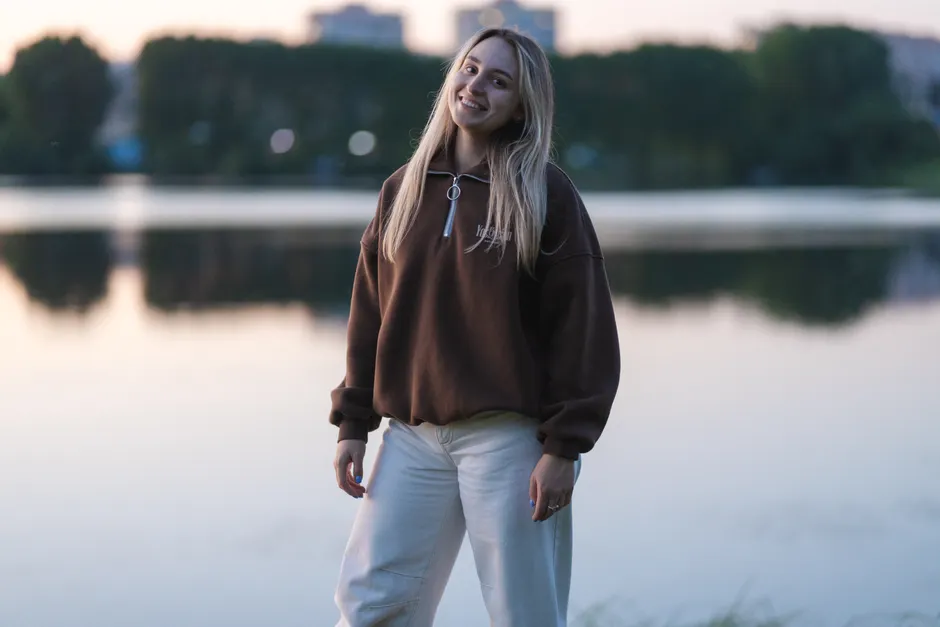 Femme souriante portant un pull quarter zip marron au bord d'un lac au crépuscule
