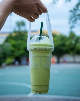 A hand holds a refreshing avocado smoothie outdoors, perfect for a healthy lifestyle.