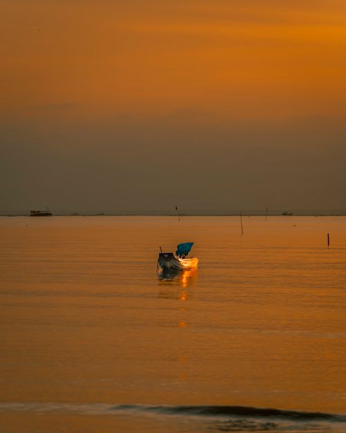 Free A peaceful fishing boat on calm waters during a vibrant sunset, creating a tranquil and warm atmosphere. Stock Photo