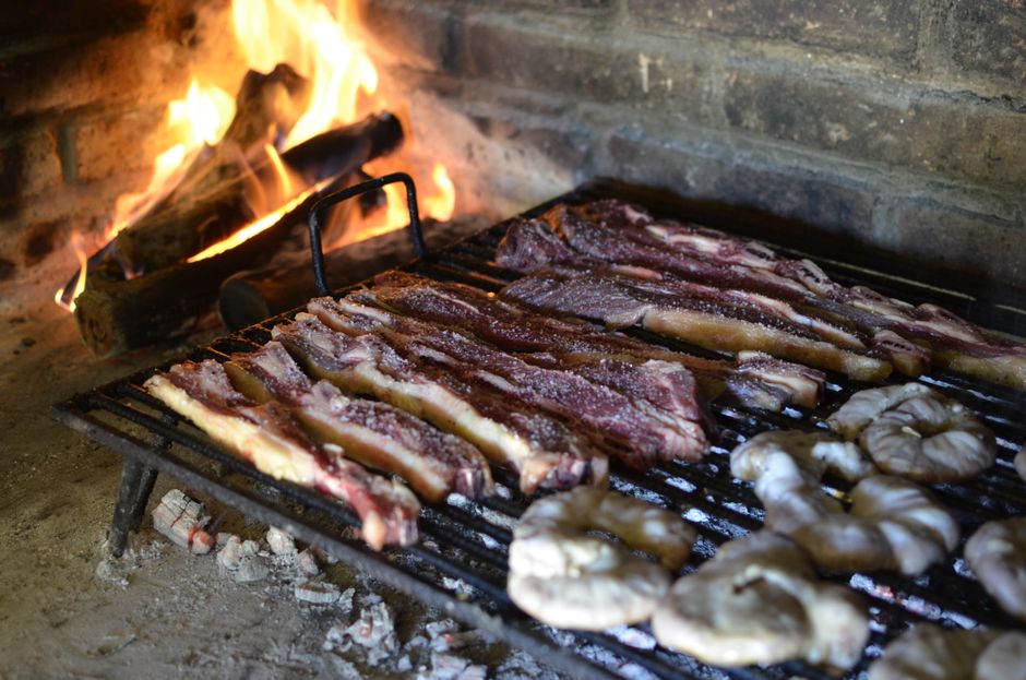 Fotomural Jugosos cortes de carne chisporroteando en una parrilla argentina tradicional con llamas abiertas.