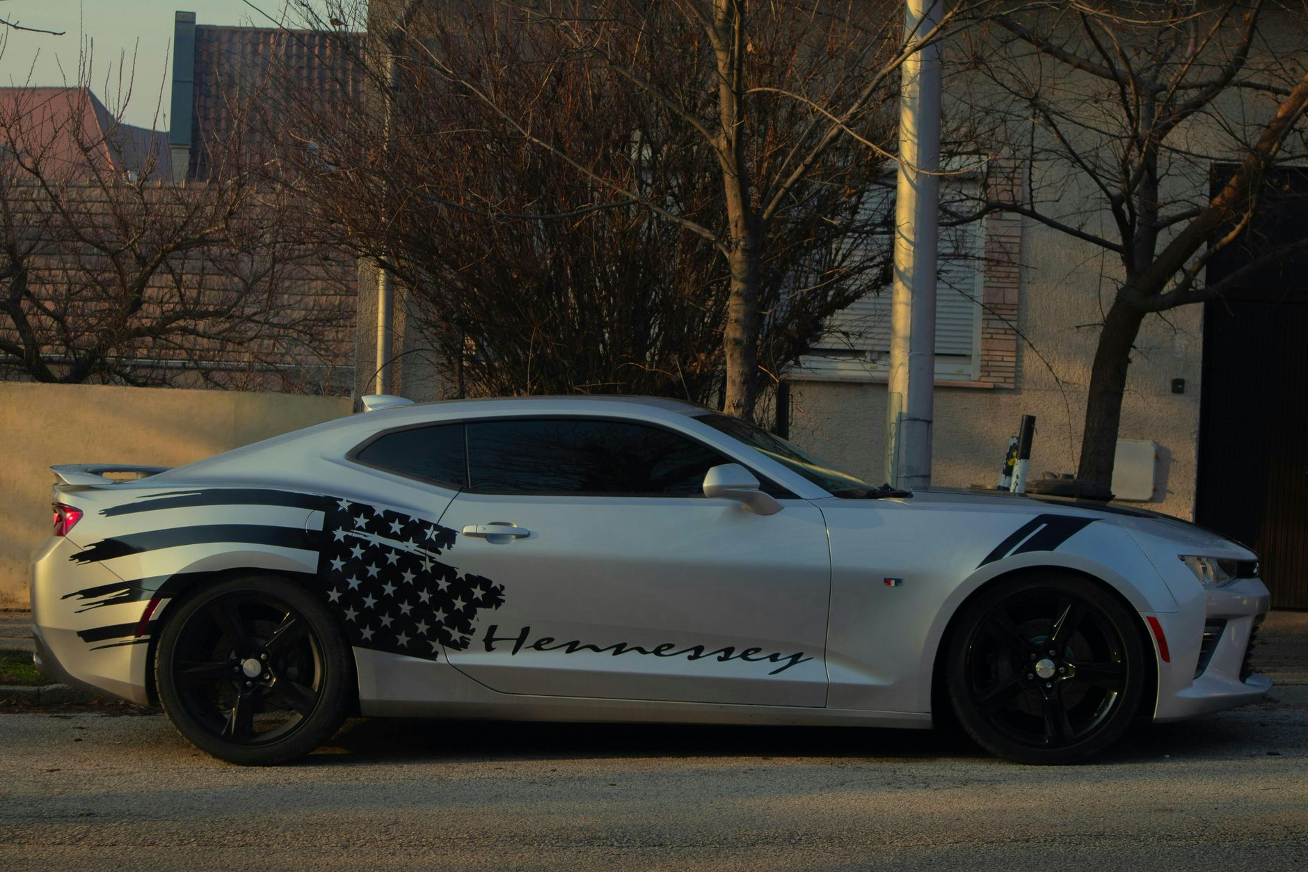 Sleek sports car with American flag design parked on urban street during daytime.