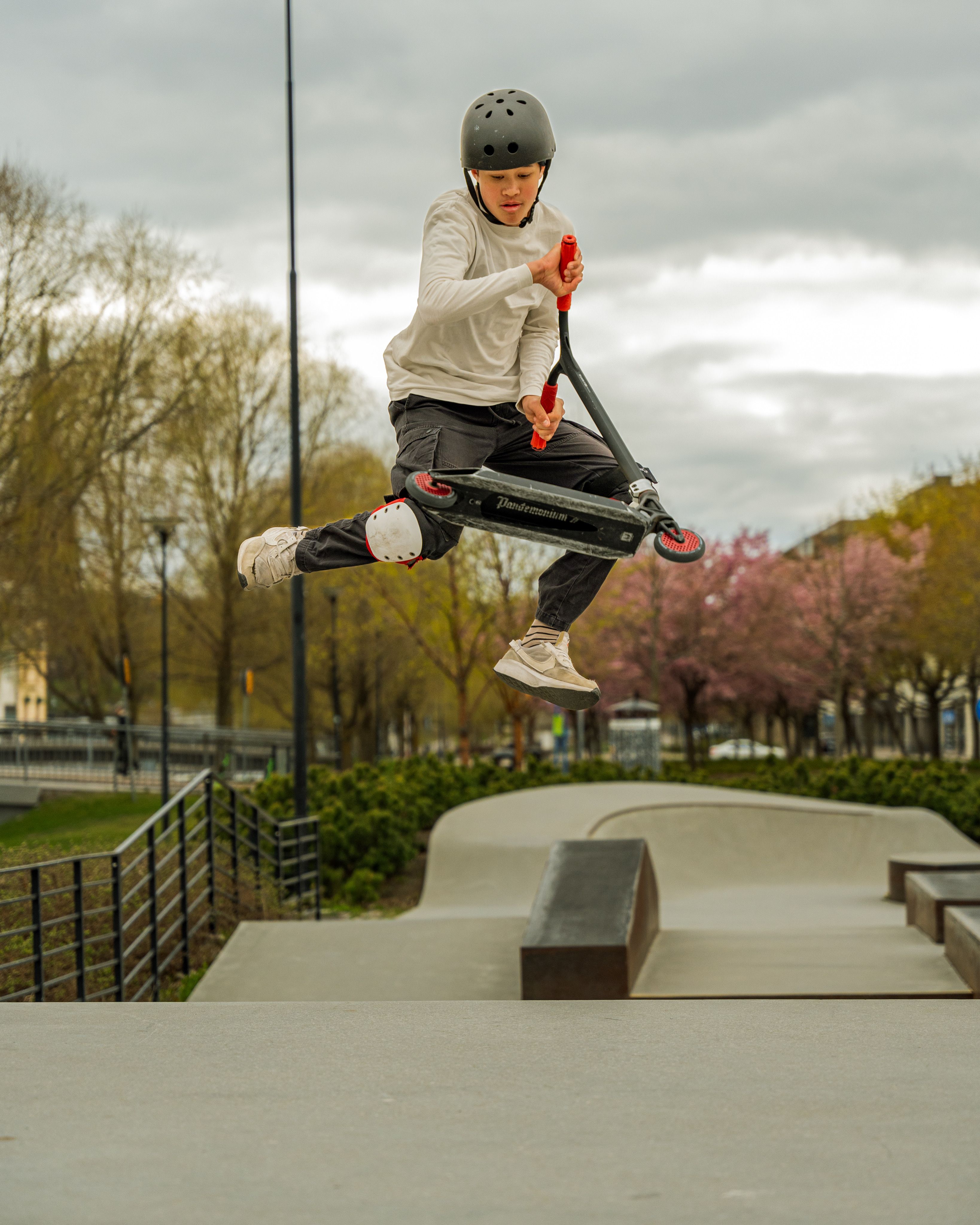 A young skater performs an aerial scooter trick at a park in Sweden, showcasing skill and balance.