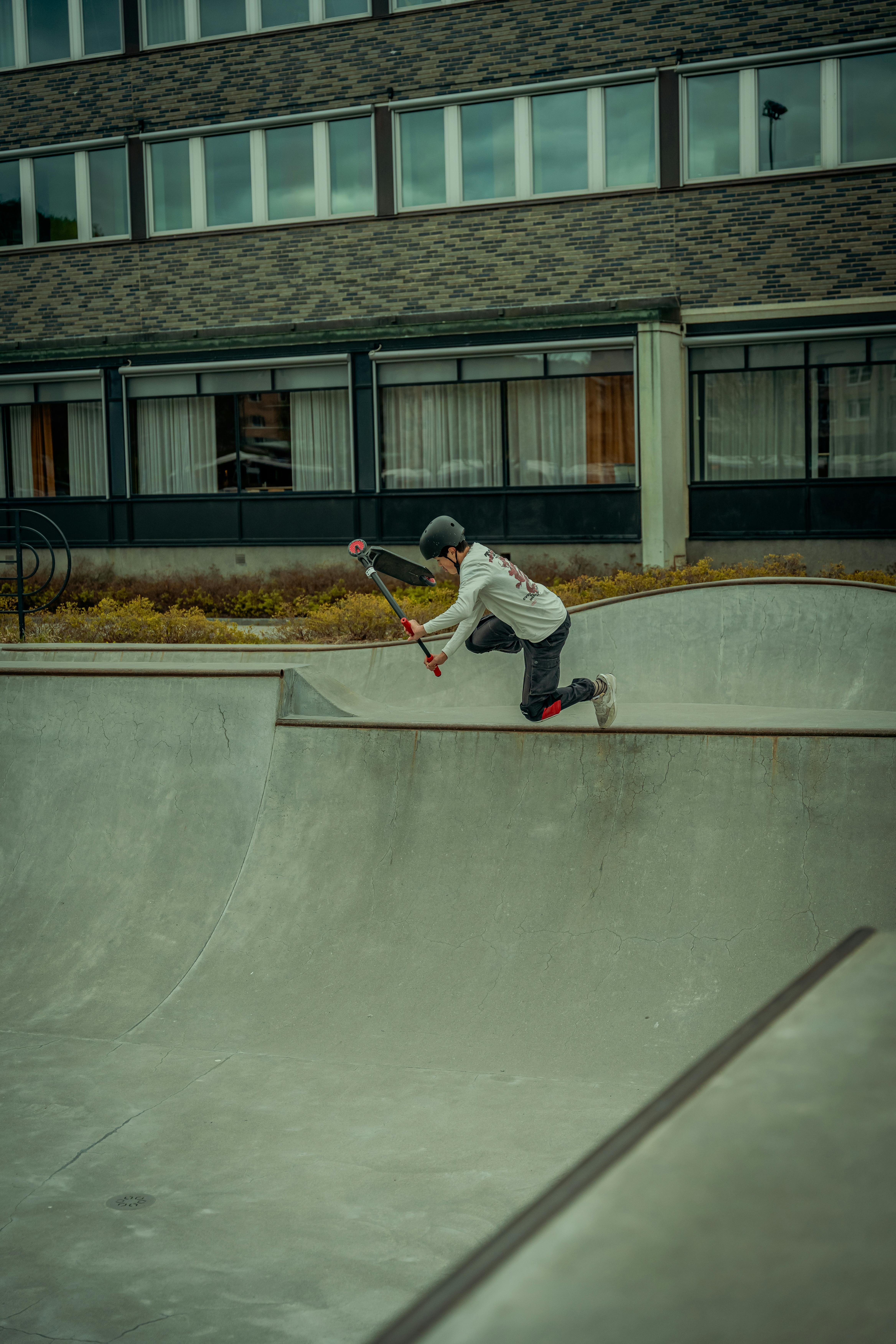 Teenage boy executing a dynamic scooter trick at an outdoor urban skatepark, showcasing skill and agility.