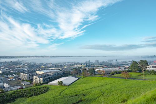 Free Aerial view of a fog-covered New Zealand cityscape with lush greenery and clear blue skies. Stock Photo