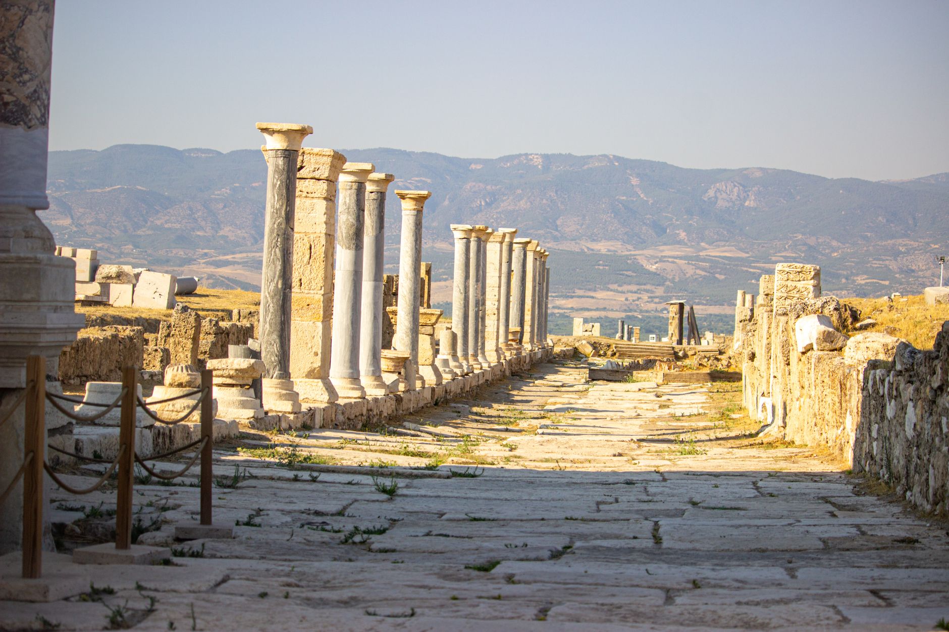 Explore this ancient Roman road in ruins with marble columns, set against a picturesque mountain backdrop.