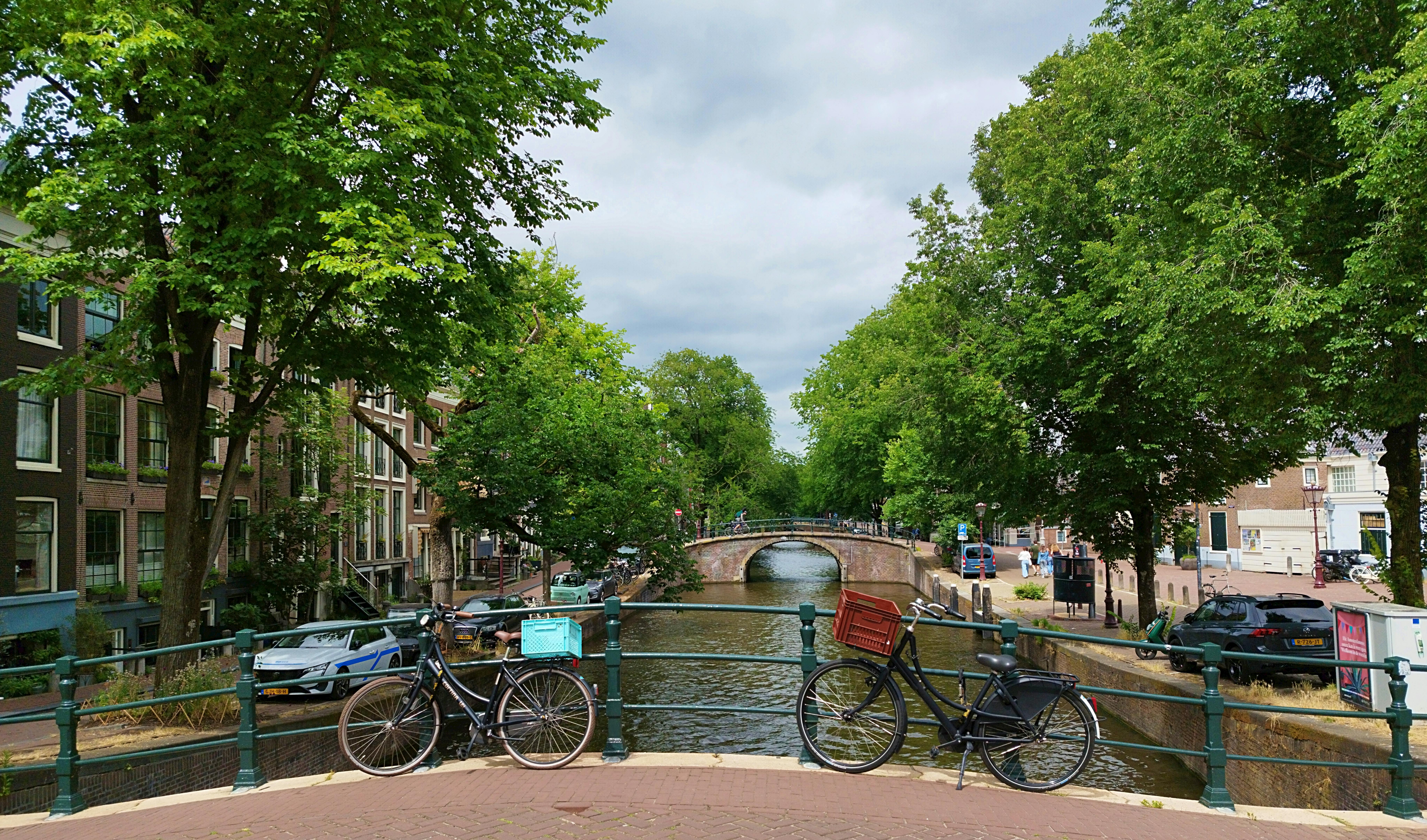Scenic view of bicycles on a bridge overlooking a canal in Amsterdam, lined with trees and historic buildings.
