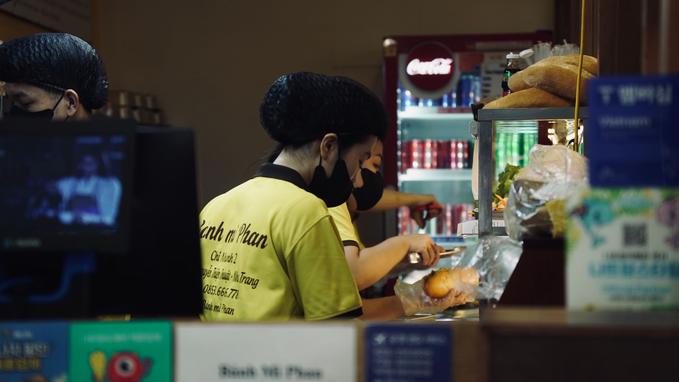 Workers prepare food at a Vietnamese street food stall indoors with vibrant signs.