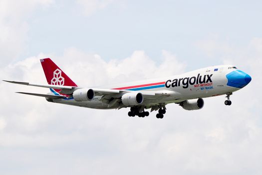 A Cargolux cargo plane flying against a blue sky with cloud backdrop.