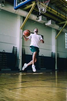 Dynamic shot of an athlete poised to dunk a basketball in a well-lit indoor court.