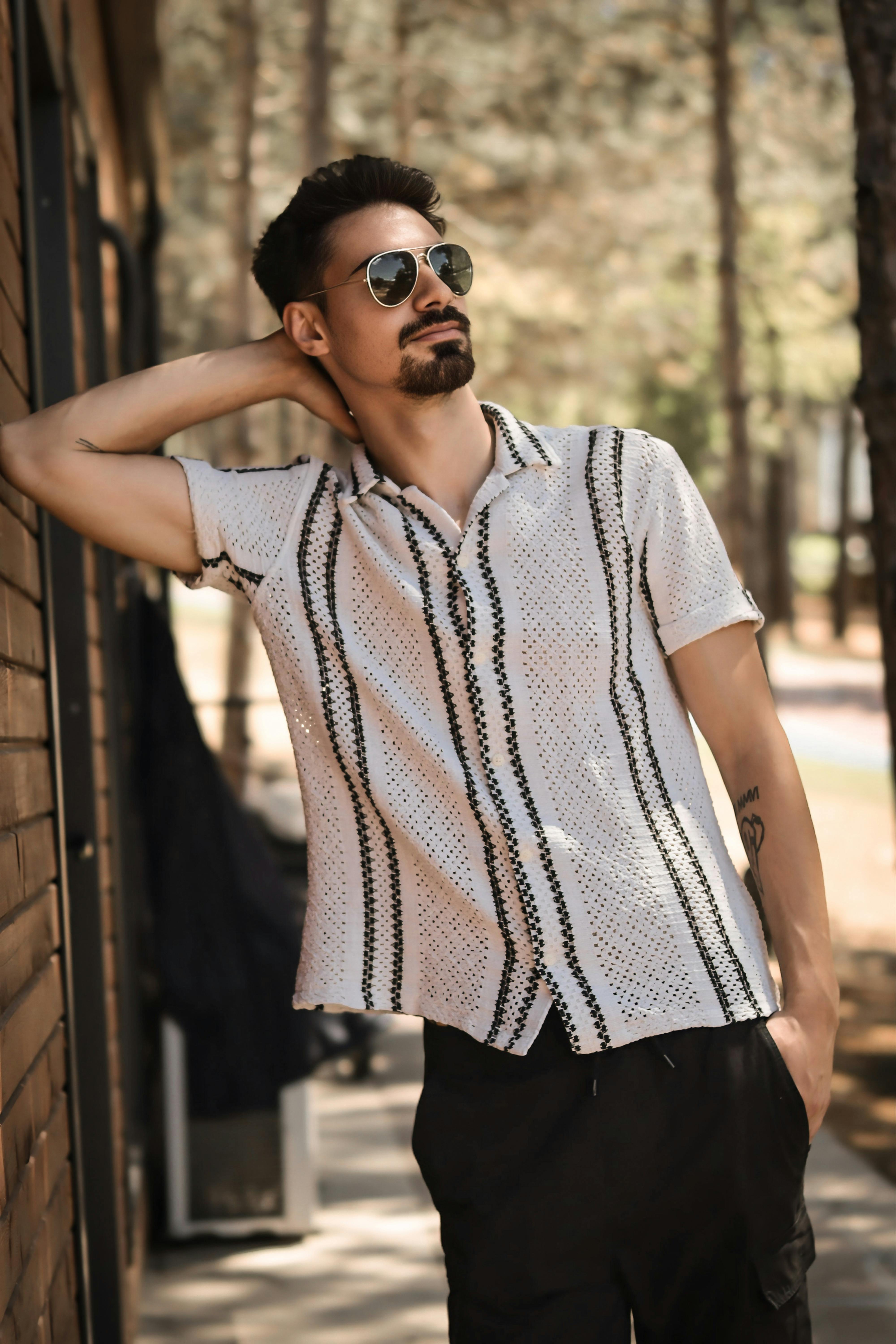 Casual young man in sunglasses posing confidently in a sunny outdoor setting.