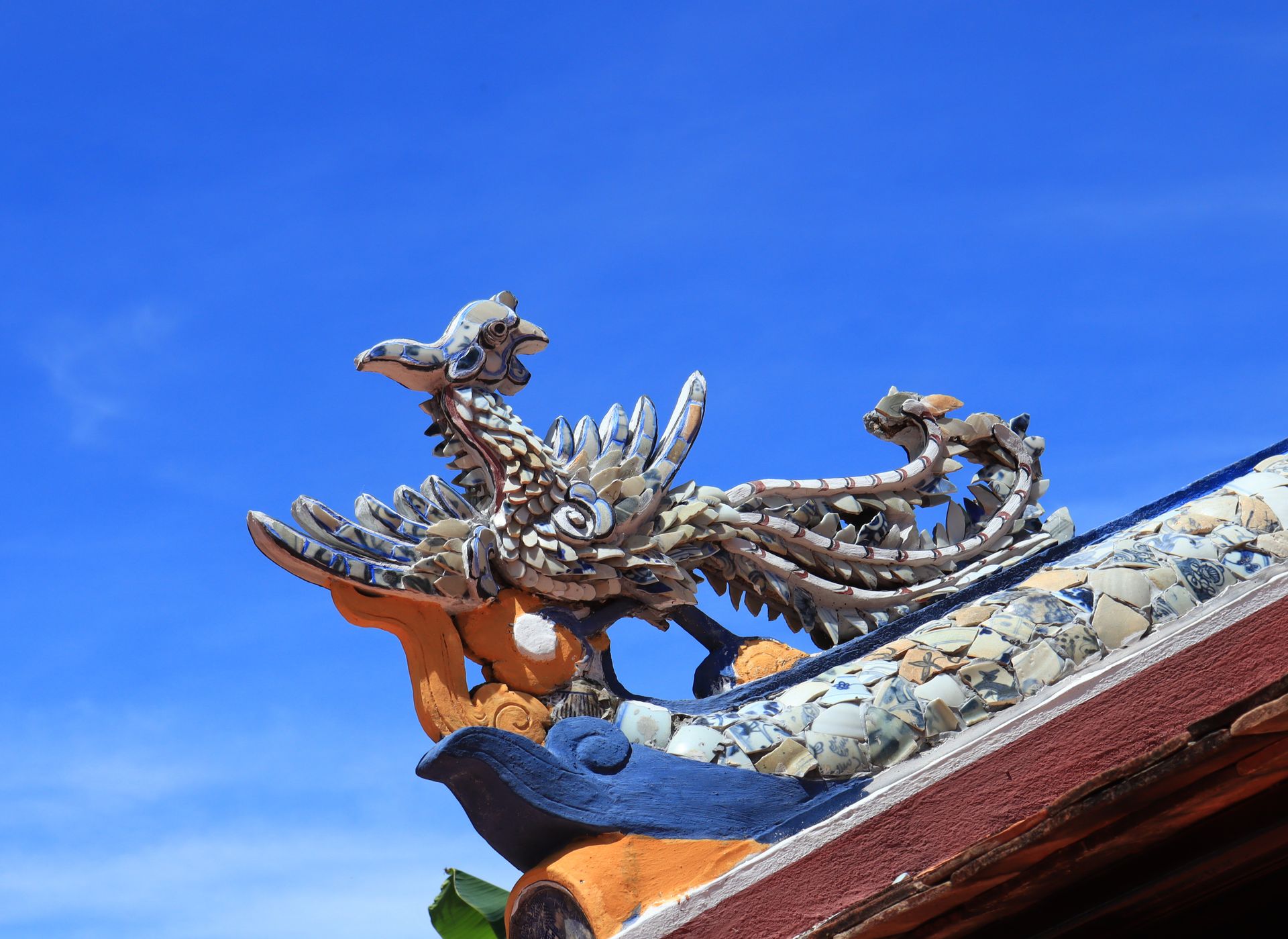 Close-up of a decorative dragon sculpture on an Asian roof with a clear blue sky.