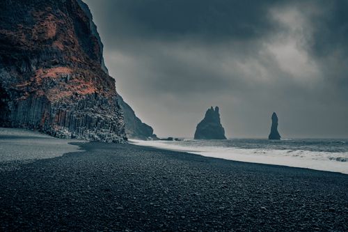 Free A moody landscape of Reynisfjara Beach with basalt columns, black sand, and sea stacks in Iceland. Stock Photo