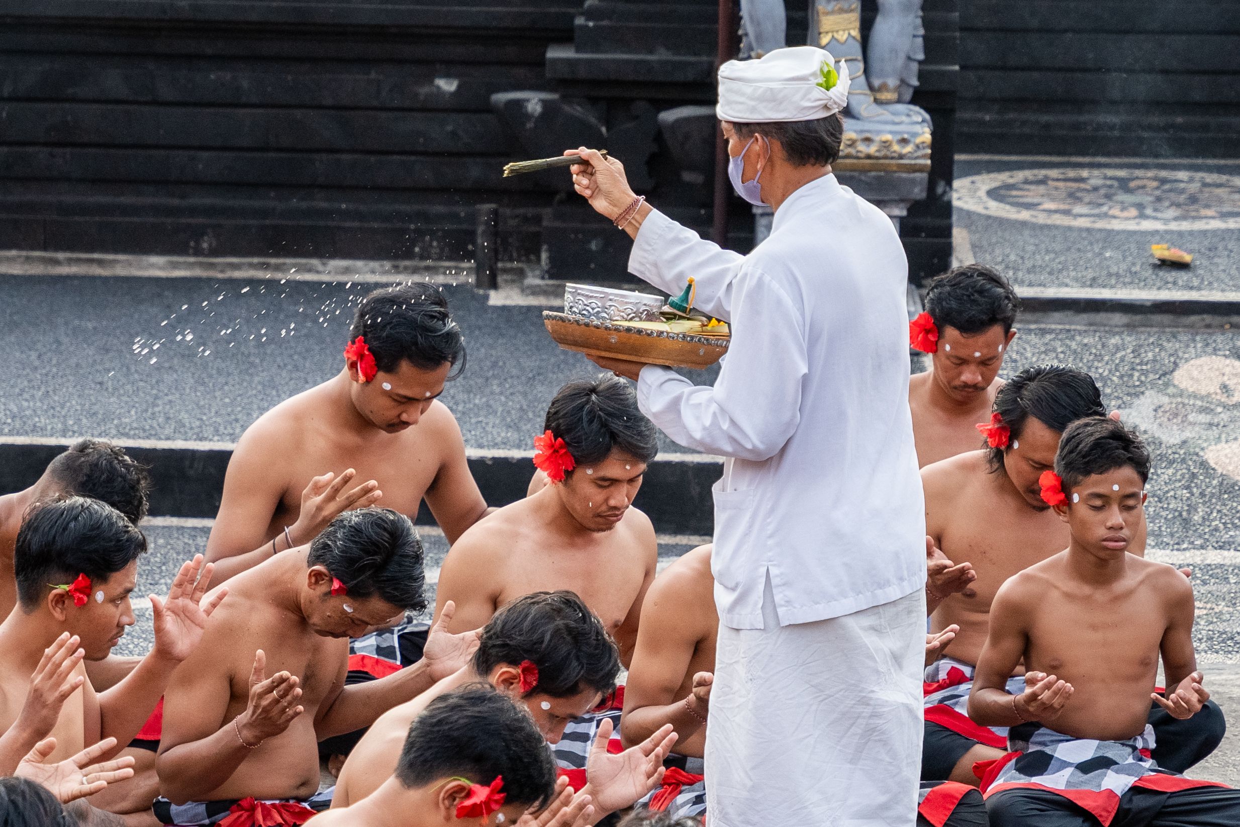 A Balinese priest performs a water blessing ceremony for young men in traditional attire.