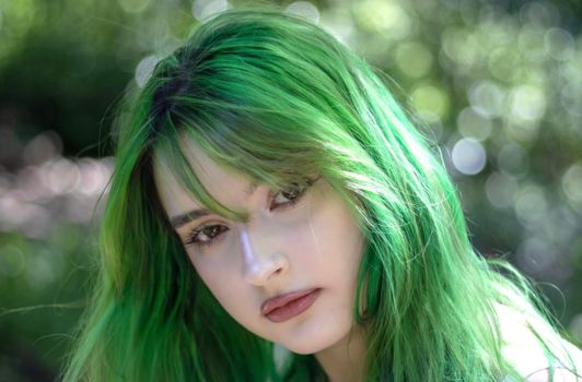 Close-up of a young woman with vibrant green hair in a natural setting.
