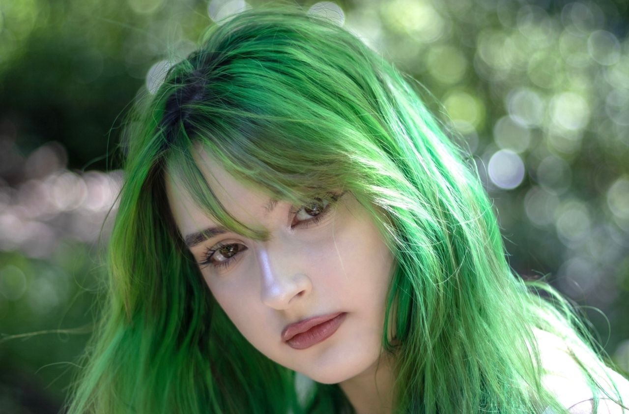 close up of a young woman with vibrant green hair in a natural setting