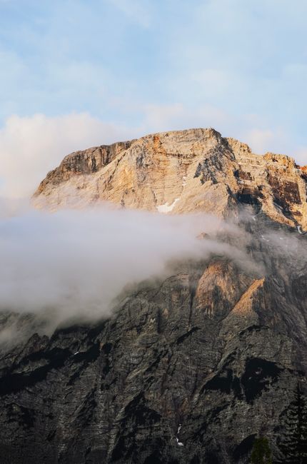 A stunning view of a mountain peak surrounded by clouds at sunrise, capturing the natural beauty and serenity.