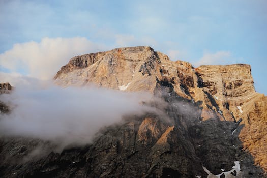 Stunning view of a rocky mountain summit shrouded in mist and clouds at sunrise.