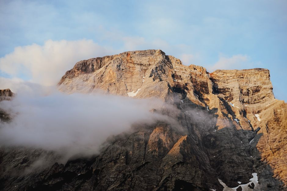 Stunning view of a rocky mountain summit shrouded in mist and clouds at sunrise.