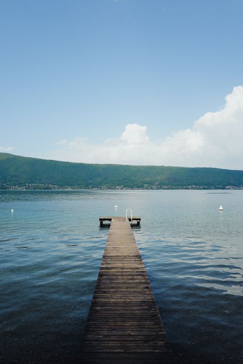 Free A tranquil wooden pier stretching into a serene lake under a clear blue sky, perfect for relaxation and escape. Stock Photo