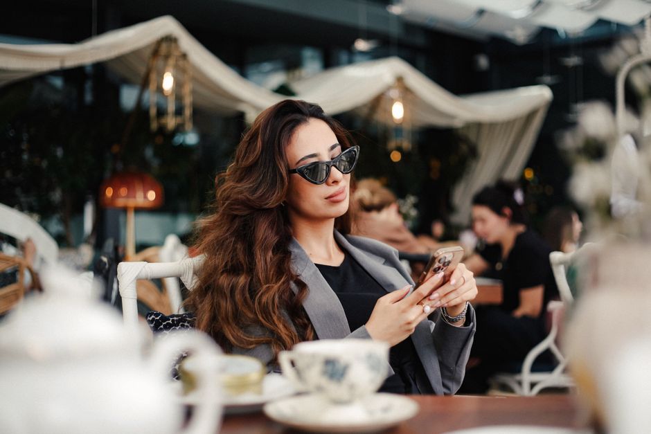 Stylish woman in sunglasses using phone at a trendy café in Baku, Azerbaijan.